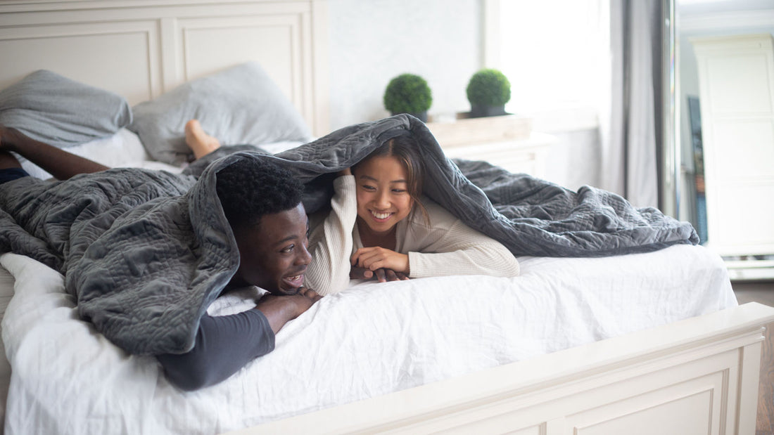 A couple smiling while covered in Hush Classic weighted blanket in bed.