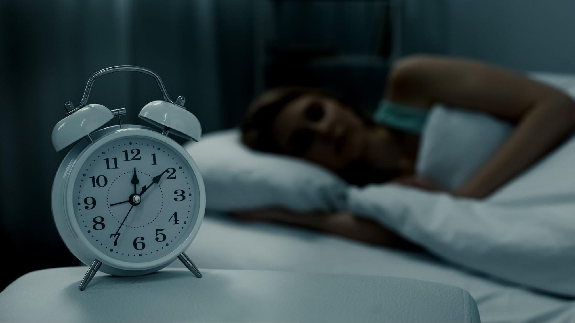 how to make yourself tired: Woman sleeping with an alarm clock on her side table