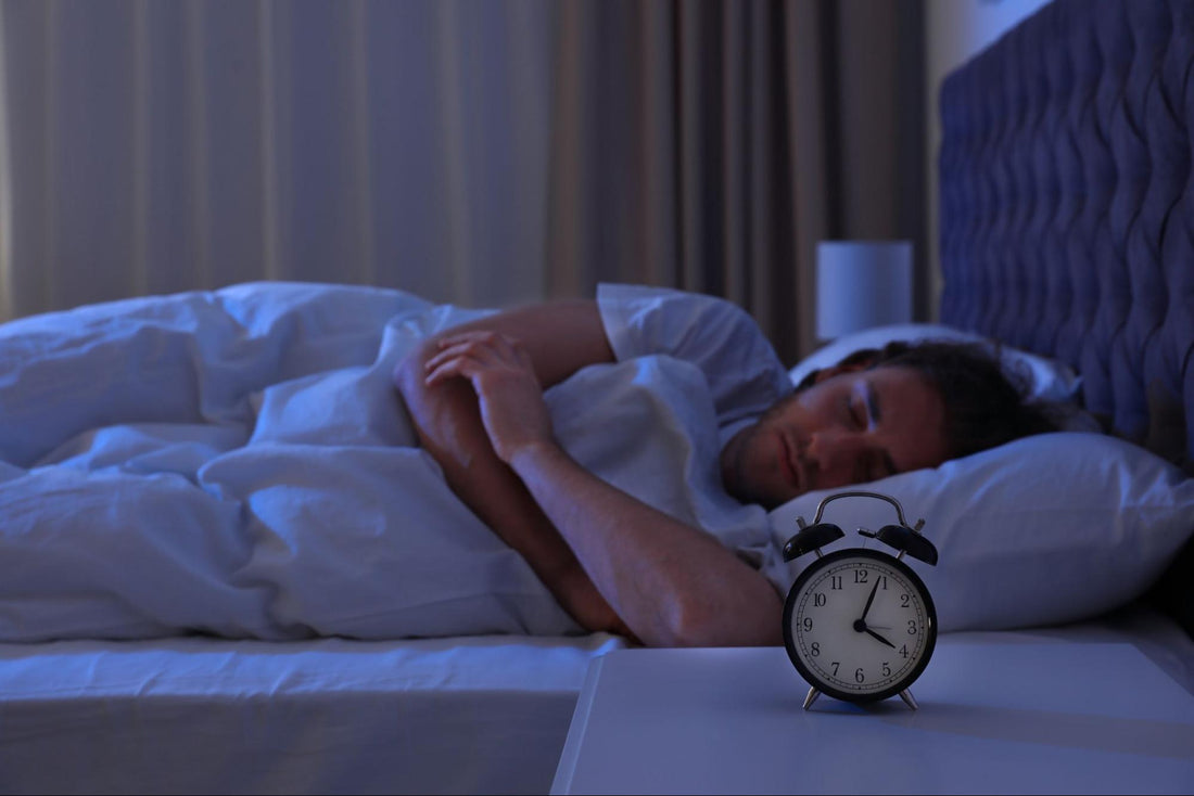 how to stay asleep: Man sleeping with an alarm clock on his nightstand