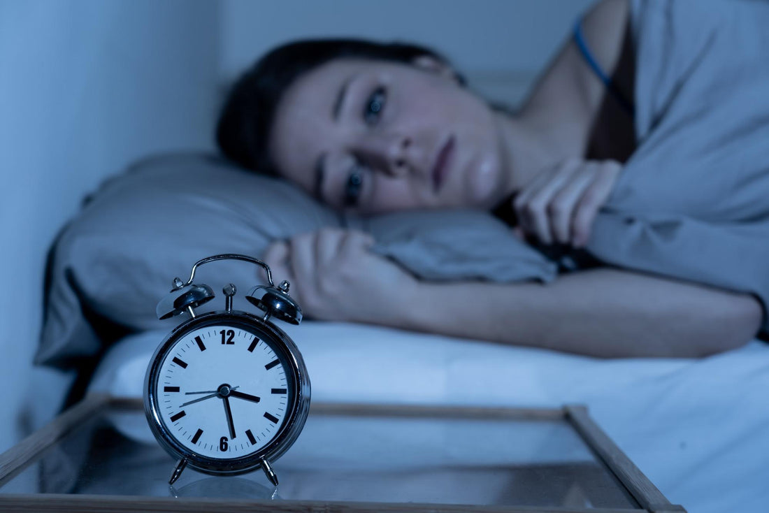 nighttime anxiety: Woman lying in bed while staring at her alarm clock