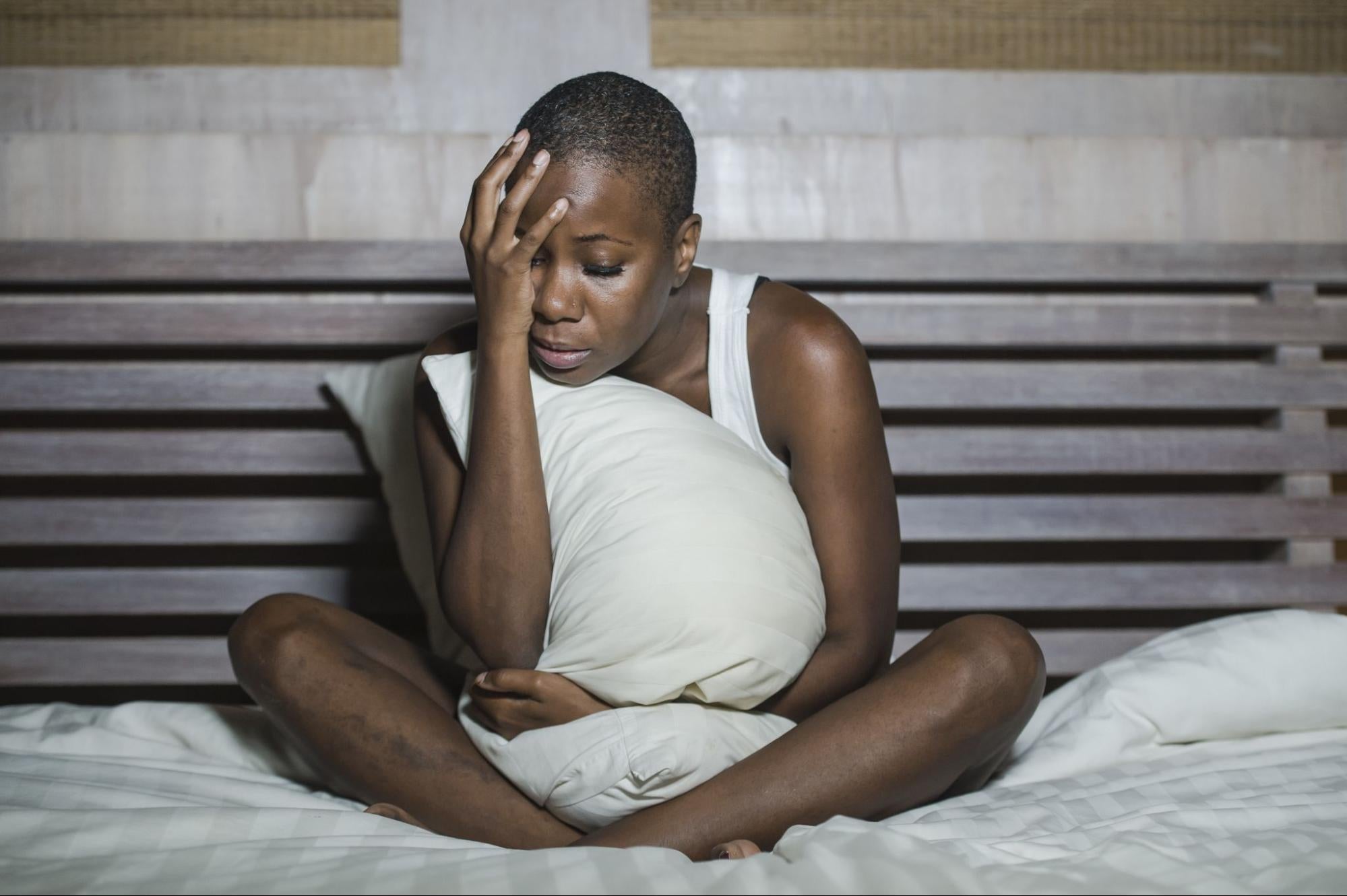 panic attacks at night: Woman sitting in bed and hugging a pillow while holding her head with her eyes closed