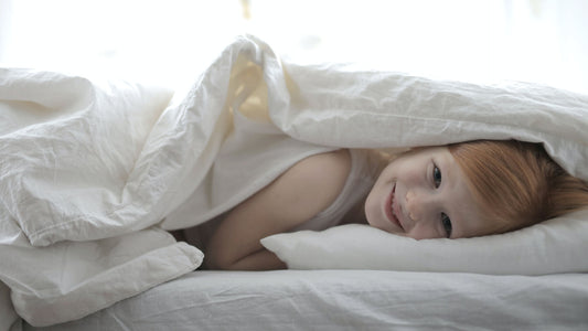A young girl smiling while lying on bed covered with white blanket.