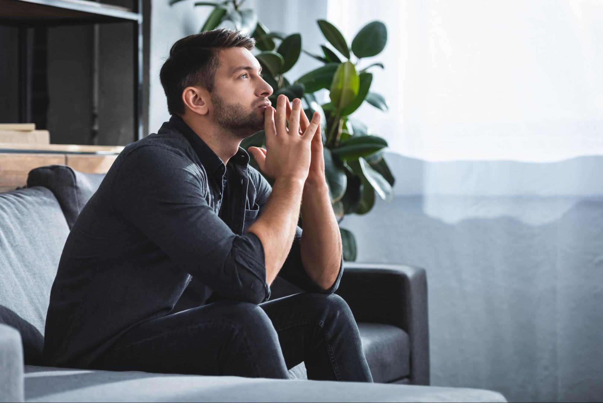 how to manage anxiety without medication: Man looking deep in thought while sitting on a couch