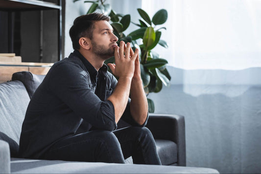 how to manage anxiety without medication: Man looking deep in thought while sitting on a couch