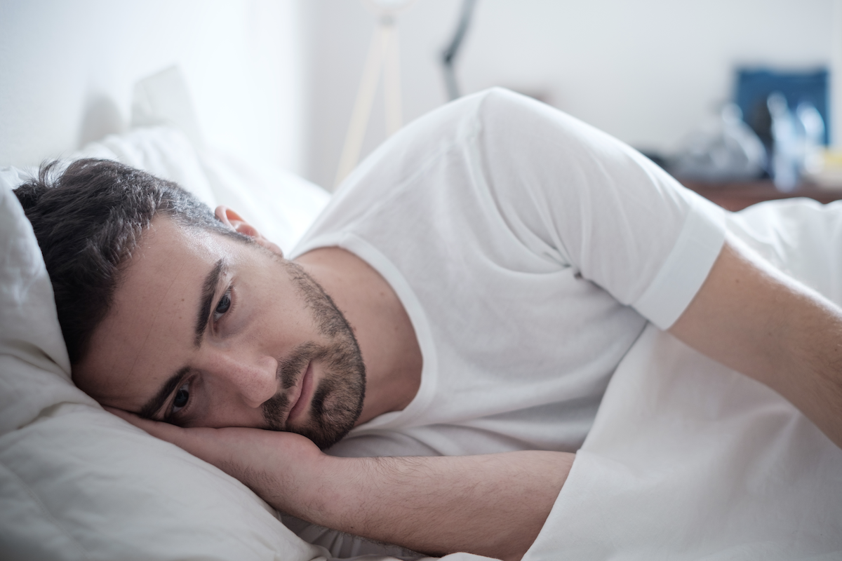 how to sleep when stressed: Stressed man looking deep in thought while lying in bed